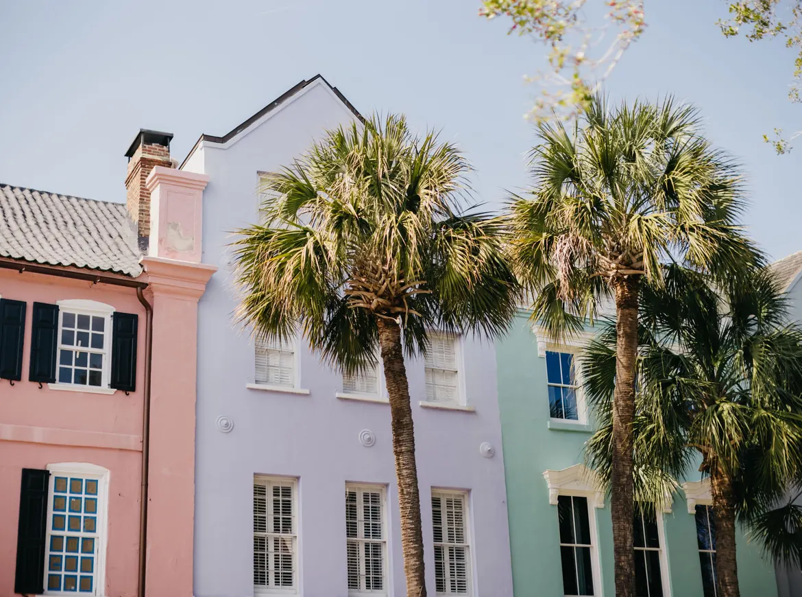 Pastel houses in pink, lavender and green with white window frames, and palmetto trees in front under a pale sky